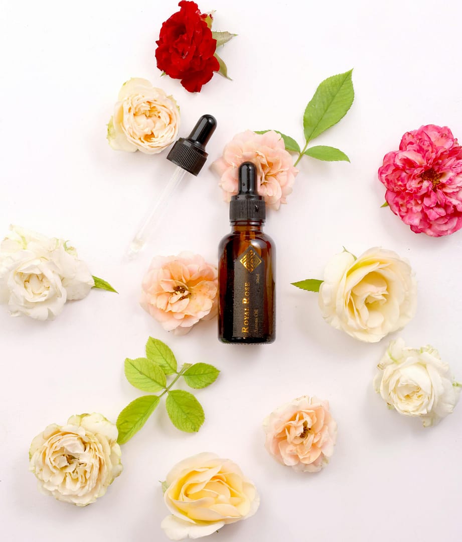 Flat lay of aromatherapy oil bottle surrounded by fresh roses and leaves for a touch of luxury.